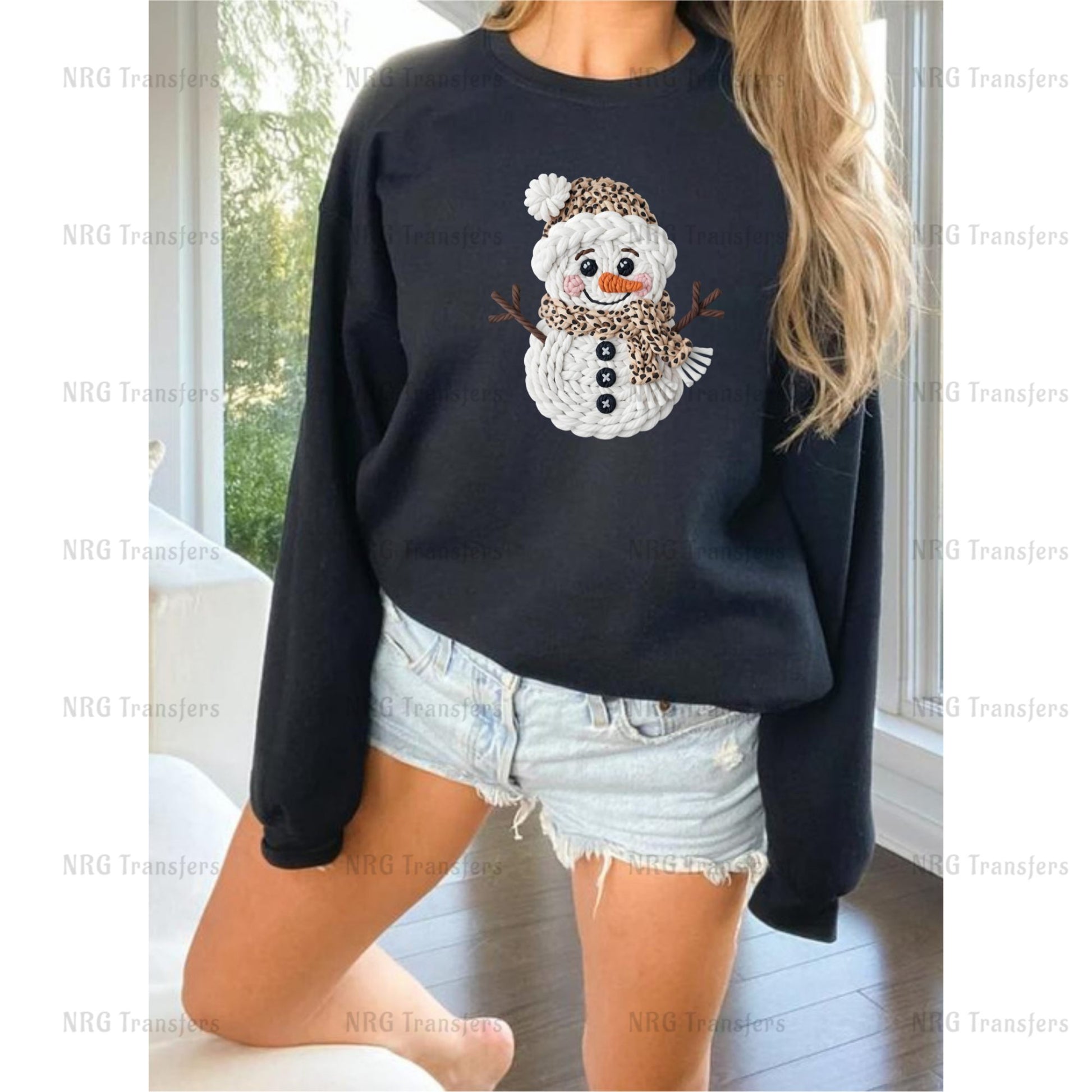 A woman wearing a black sweatshirt with a snowman design on it, paired with denim shorts.
