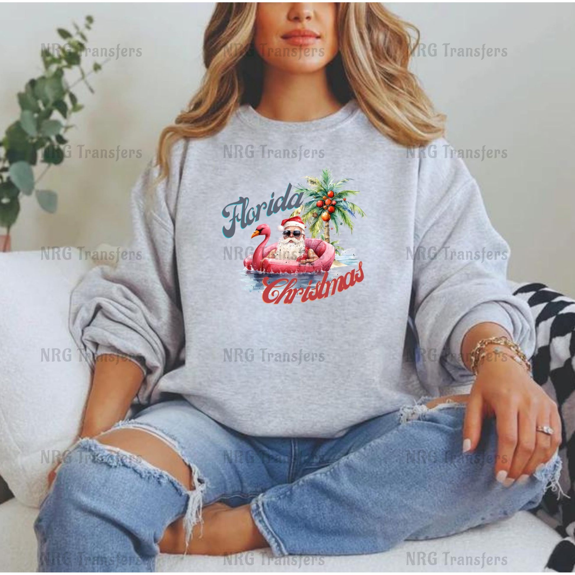 A woman wearing a gray sweatshirt with a graphic of a flamingo and palm tree, sitting on a couch.