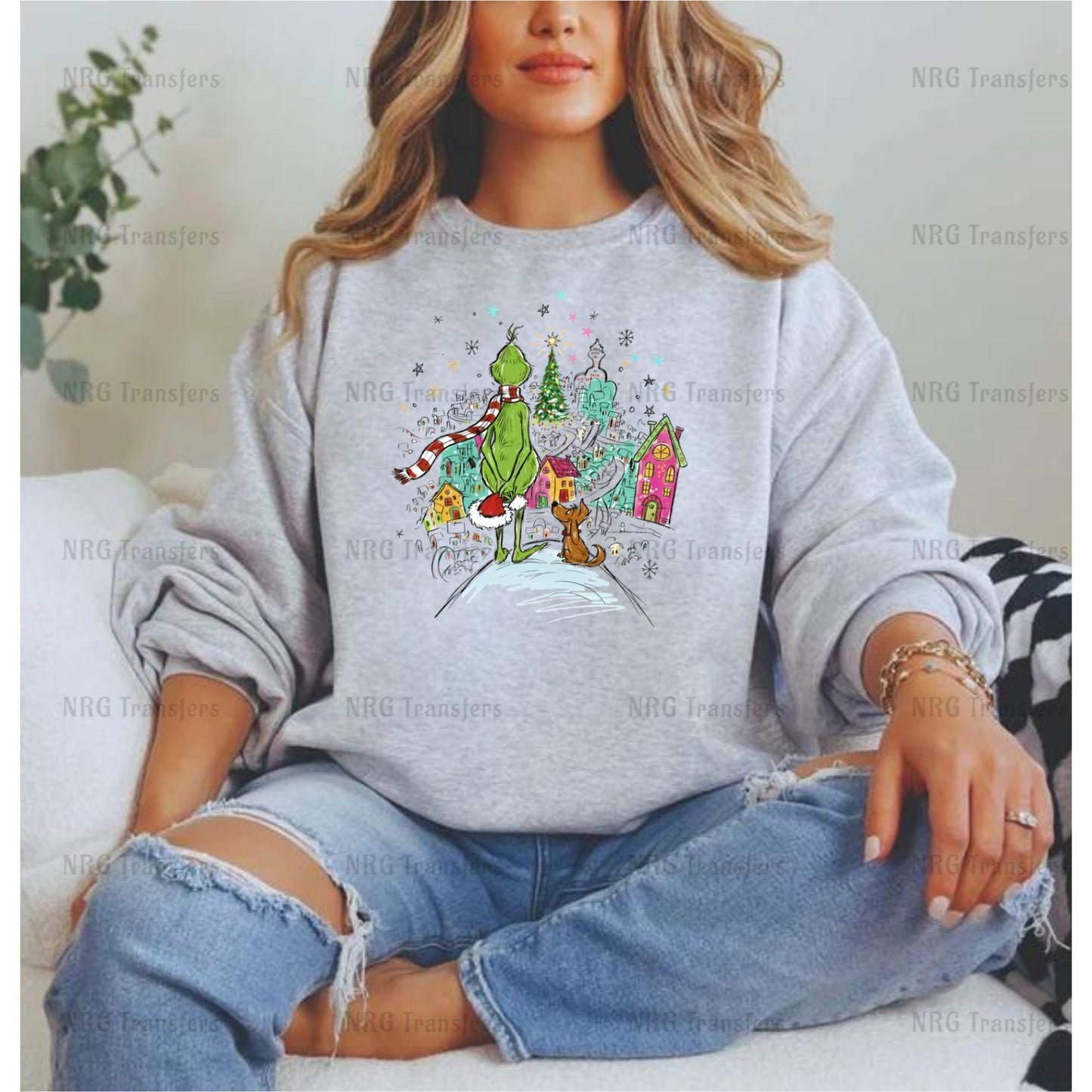 A woman wearing a gray sweatshirt with a colorful graphic of a Christmas village and a Grinch on it.